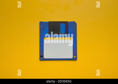 Blue 3.5-inch floppy disk with a blank white label on a bold, contrasting yellow surface. Stock Photo