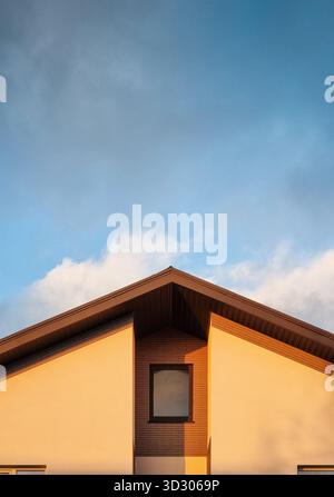 The gable end of a house with a recessed window. Detail of modern countryside house at sunset, cloudy house in the background. Stock Photo