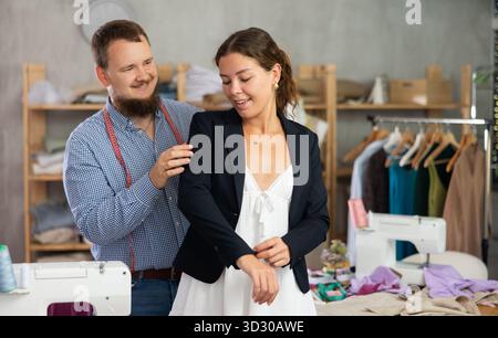 Female client trying on custom blazer with tailor in workshop Stock Photo