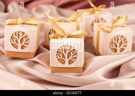 Many beige and brown gift boxes with golden ribbons on the beige silk background. The group of gift boxes with tree decoration. Stock Photo