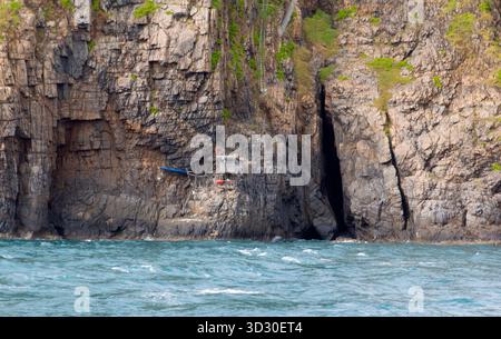 Small hut built on steep sea cliffs at Con Dao, Vietnam, facing rough ocean waves and rocky coastline. Stock Photo