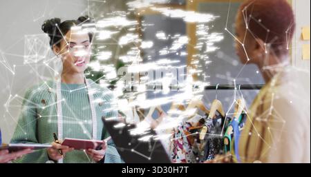 Discussing designer holding pink notebook with pencil by clothing rack in design studio, copy space Stock Photo