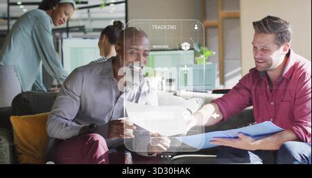Examining two men collaborating on documents with blue clipboard in office lounge, with AR overlay Stock Photo