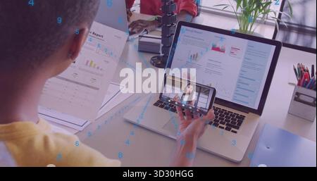 Man in yellow tee analyzing charts holding smartphone and annual report at office desk, with laptop Stock Photo