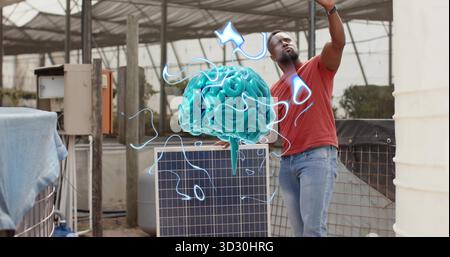 Raising arm male technician leaning on solar panel in greenhouse toward turquoise brain hologram Stock Photo
