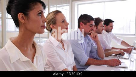 Sitting five professionals in business casual at office meeting room, with notebooks and laptops Stock Photo