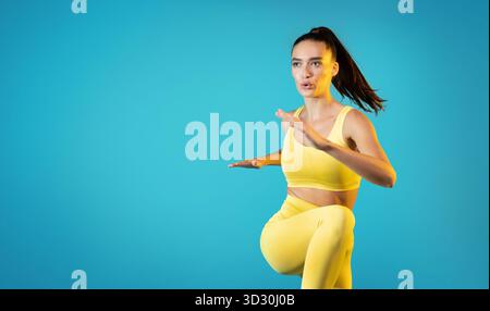 Fit Young Lady Performs Elbow to Knee Crunch in Bright Studio Against Blue Background Stock Photo