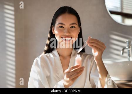 Smiling Korean Woman Showcases New Beauty Serum in Her Morning Routine at Home Stock Photo