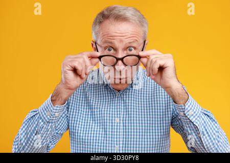 Surprised Mature Man Expresses Shock at Unexpected News Against Bright Yellow Background Stock Photo
