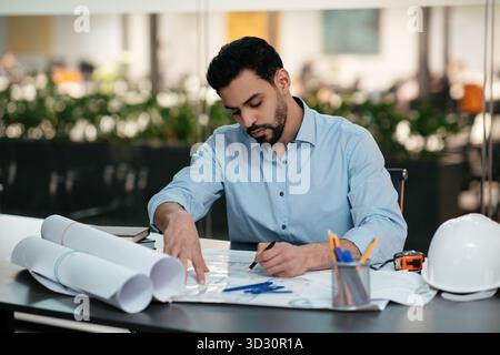 Engineer Working on Blueprint Designs in a Modern Office Space During Daylight Hours Stock Photo