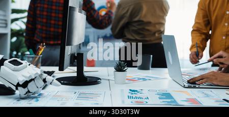 A dynamic office scene showcasing teamwork as diverse professionals engage in brainstorming, analyzing data on charts, and utilizing digital devices f Stock Photo