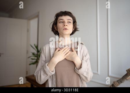 Young woman practicing stress relief, doing breathing exercises for calming, holding hands on chest. Stock Photo