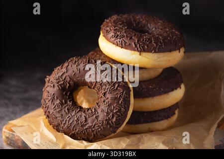 A stack of chocolate-covered donuts with sprinkles rests on parchment paper, showcasing a tempting treat in a warm and inviting atmosphere ideal for d Stock Photo