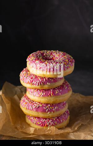 A tall stack of five pink frosted donuts covered in colorful sprinkles sits on crumpled brown parchment paper. The enticing arrangement highlights the Stock Photo