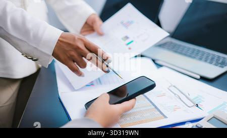 Close-up of business team analyzing financial data charts and discussing strategy with smartphone and documents on desk. Concept of teamwork, finance, Stock Photo