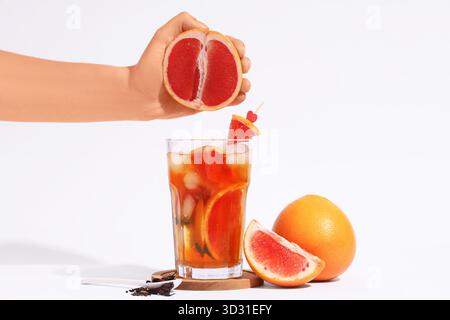 Young woman squeezing grapefruit juice into glass of tasty cold ice tea on white background Stock Photo