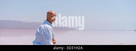 Man is standing on the beach with his arms crossed. He is wearing a white shirt. The beach is near the ocean Stock Photo