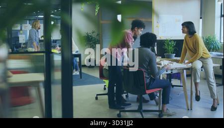 Discussing project team reviewing scale model in open-plan office with whiteboard and plants Stock Photo