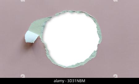 Circular irregularly torn hole in sheet of matte, dusty rose or muted pink cardboard paper. Edges of tear rough. Central space blank white and soft sh Stock Photo