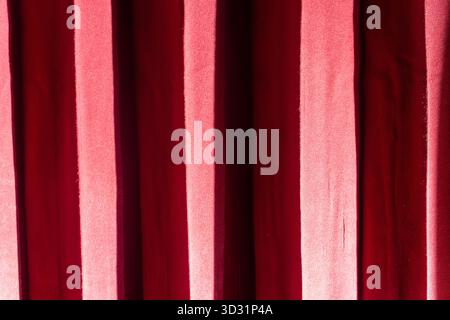 A close-up of a red curtain. The fabric folds create a pattern of light and shadow. Concept for theater, cinema, stage, or a luxury background. Stock Photo