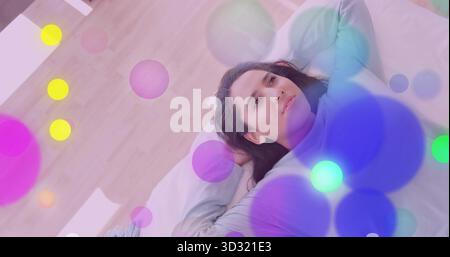 Reclining woman gazing upward on bed in bedroom at home, with pillow and abstract colored circles Stock Photo