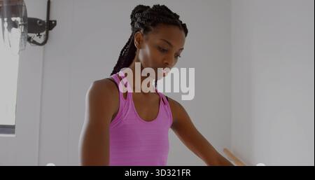 Practicing dancer in purple tanktop aligning arms at barre in studio, with fan and window frame Stock Photo