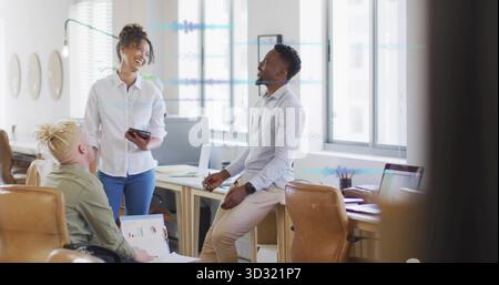 Collaborating professionals reviewing laptop charts and smartphone in open office with wooden desks Stock Photo