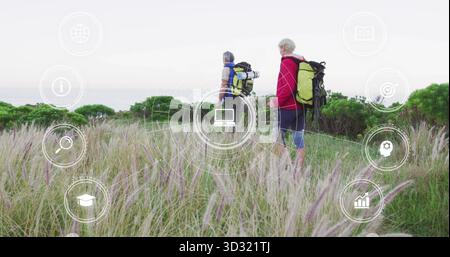 Walking couple wearing hiking gear along coastal dune footpath, with backpacks, rolled sleeping mat Stock Photo