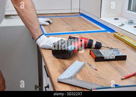 repairman working on a new kitchen installation and using electric drill Stock Photo