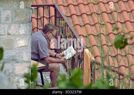 person reading a book sitting on the the balcony, Perast, Montenegro Stock Photo