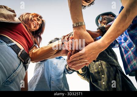 A low-angle view of a happy, multicultural group of young friends stacking their hands together in a huddle, symbolizing teamwork and unity. Stock Photo