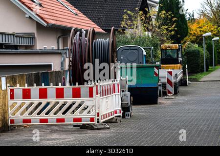 Heavy machinery and construction barriers are seen on a street in a residential neighborhood. Cable reels are placed nearby, indicating ongoing utilit Stock Photo