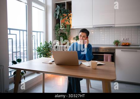Mature woman smiling while on business call, work on laptop at home. Remote work, self employed job Stock Photo