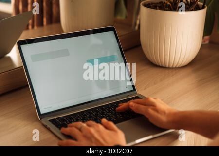 AI chat on laptop at home desk, hands typing Stock Photo