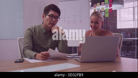 Reviewing documents, using laptop and smartphone, Asian man and woman collaborating in meeting room Stock Photo