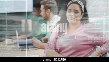 Woman wearing pink sweater and headband reviewing projected code in office, with laptops Stock Photo