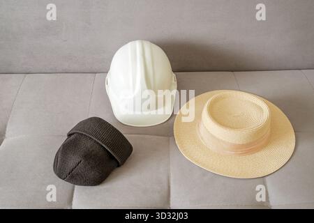 knitted hat, construction helmet and straw hat on sofa Stock Photo