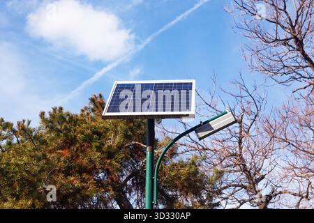 A solar panel is installed on a street lamp post in a park Stock Photo
