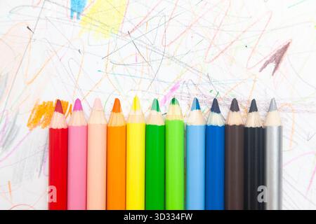 Multi-colored pencils lie on white paper drawn with multi-colored curved lines Stock Photo