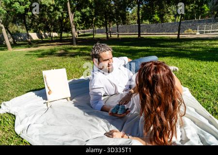 Couple laying on grass showing a pair of cute baby shoes, symbolizing new parenthood Stock Photo