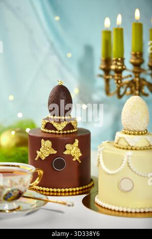 Two beautifully decorated easter cakes topped with chocolate eggs, golden angels, and beads, creating a luxurious and elegant festive scene Stock Photo