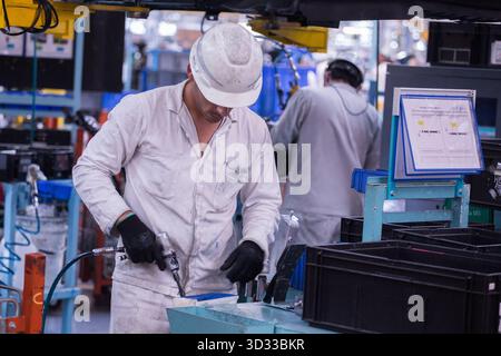 Men at work. Young man wearing protective stuff, working with tools and machinery in a car factory Stock Photo