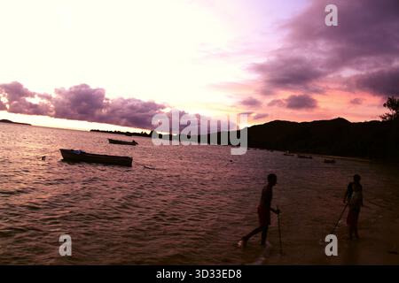 Purple skies merge with golden waves around anchored boats at sunset. Serene seascape off the coast of Praslin, Seychelles. Stock Photo