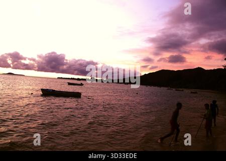 Boats drifting on glowing turquoise water under vibrant skies of pink and orange. Tropical peace in Praslin, Seychelles. Stock Photo