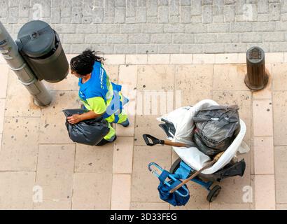 top view of spanish street cleaner collecting rubbish with a trash cart and black bags on aa road in can pastilla mallorca viewed from above Stock Photo
