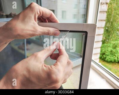 Broken mosquito screen. Repair of the mosquito net, sealing of the damaged area, holes in the net. Close up. Stock Photo