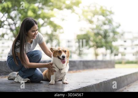 A young woman enjoys a moment of connection with her corgi, petting it affectionately in a peaceful outdoor space Stock Photo