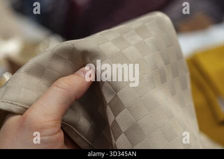 A person's hand holding up a piece of tan fabric with a repeating checkered pattern, up close Stock Photo