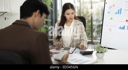Two business professionals review financial reports and calculations, discussing budget strategies and performance metrics Stock Photo