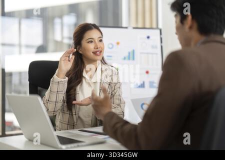 A young woman engages in a financial consultation, discussing strategies and insights with her colleague in a modern office Stock Photo